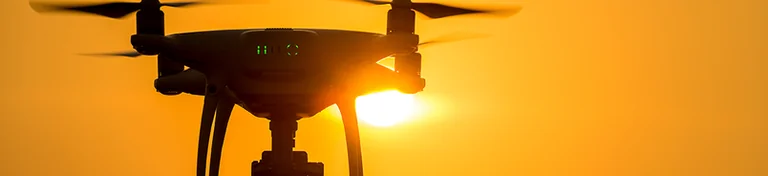 A quadcopter drone in flight at sunset