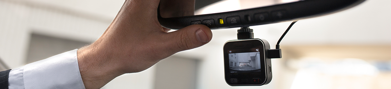 A dash camera being fitted beside a vehicle rear-view mirror